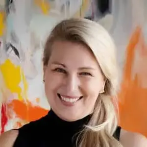 A woman with long blonde hair, wearing a black sleeveless top, smiles in front of a colorful abstract background.