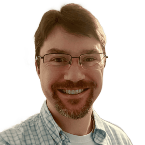 A person with glasses, a beard, and a mustache smiles at the camera, wearing a light blue checkered shirt.